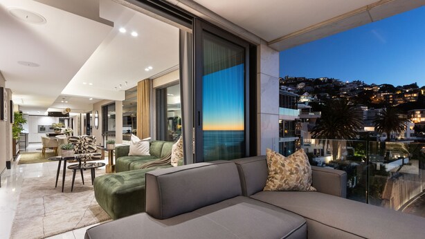A modern living room with a large sectional sofa, a glass coffee table, and a view of a cityscape at dusk. - Aurum 501 (Cape Town)