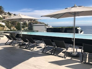 Zona de piscina con sillas de descanso y sombrillas, con vista a una masa de agua.