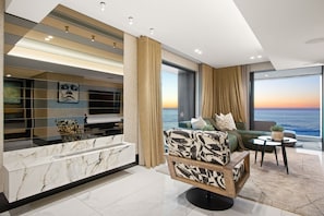 A modern living room with a marble reception desk, a sofa with patterned cushions, a small round table, and a large window with a view of the ocean. - Aurum 501 (Cape Town)