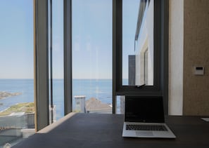 A laptop on a desk with a view of the sea and buildings through large windows. - Aurum 501 (Cape Town)