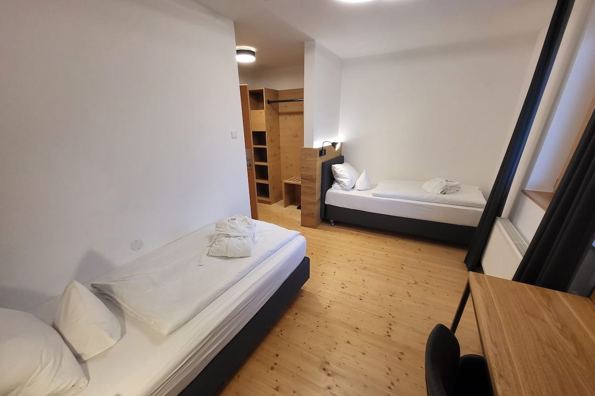 Une petite pièce, de taille modeste, comprenant deux lits, un plancher en bois et un bureau.