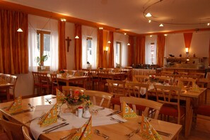 A dining area with multiple tables set for service, featuring orange curtains and a cross on the wall. - Witikohof (Haidmuhle)