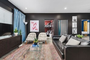 Un salon moderne comprenant un canapé, des fauteuils, une table basse et un téléviseur. On y trouve également des objets décoratifs et un tapis à motifs.