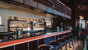 Eine Bar mit einer langen Theke, Hockern und Regalen voller Flaschen.
