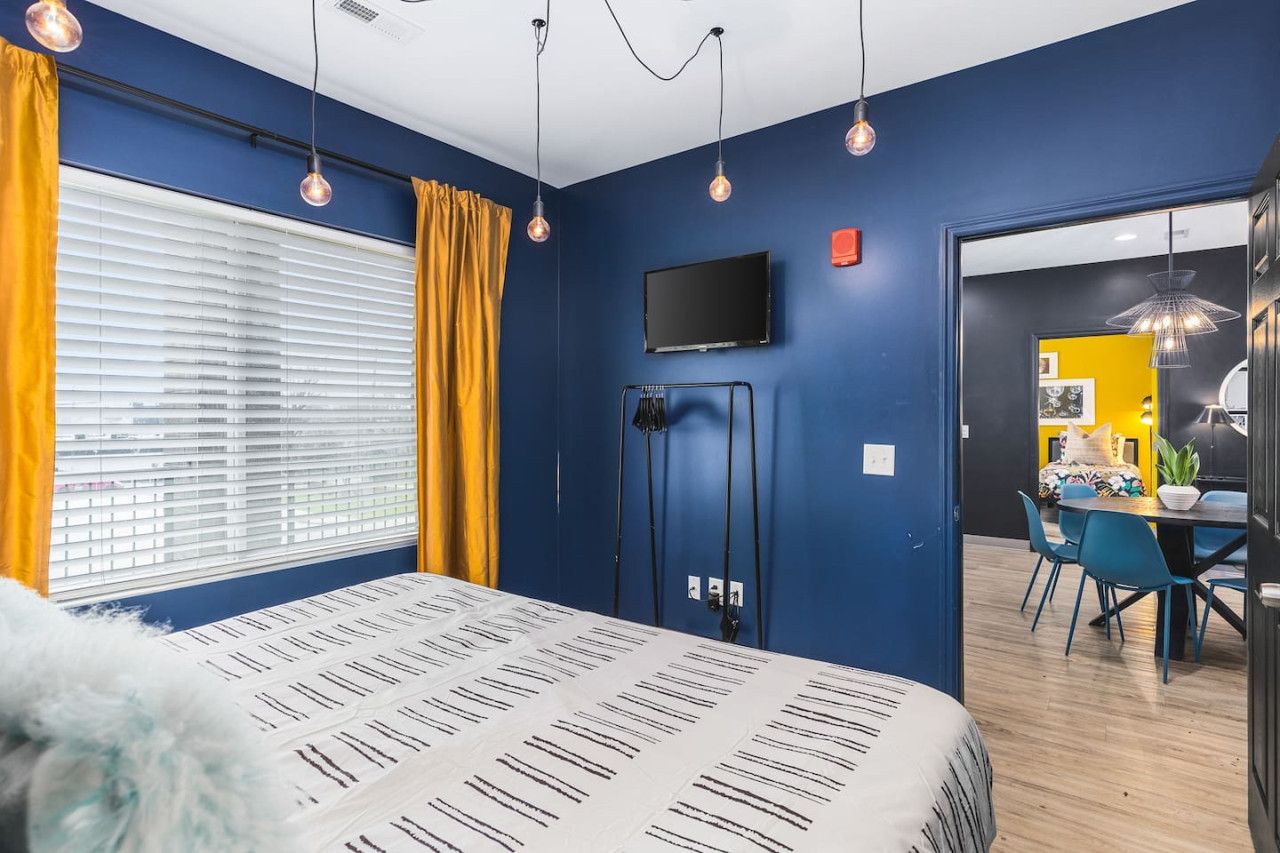 A bedroom with a bed, a TV, and a desk with chairs.