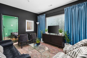 A modern living room with a flat-screen TV, a sofa, a coffee table, and a bookshelf. - Condo Near Downtown - WALK to restaurants, bars & music (Nashville)