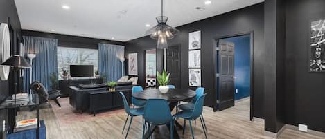 A modern living room with a black sofa, a dining table with blue chairs, and a large TV.