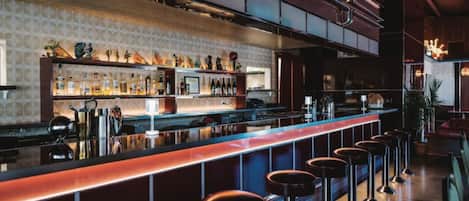 A bar area with stools, a counter, and shelves with bottles.