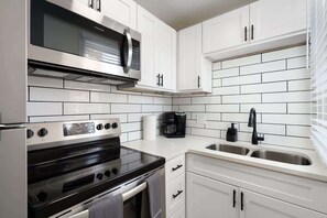 Een moderne keuken met witte kasten, een roestvrijstalen afzuigkap, een ingebouwde magnetron, een dubbele oven en een spoelbak met kraan.