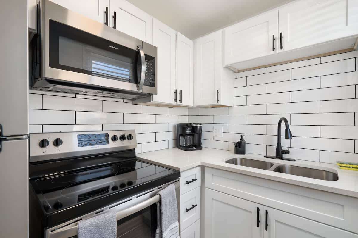 A modern kitchen with white cabinetry, a stainless steel microwave, a built-in oven, and a coffee maker.