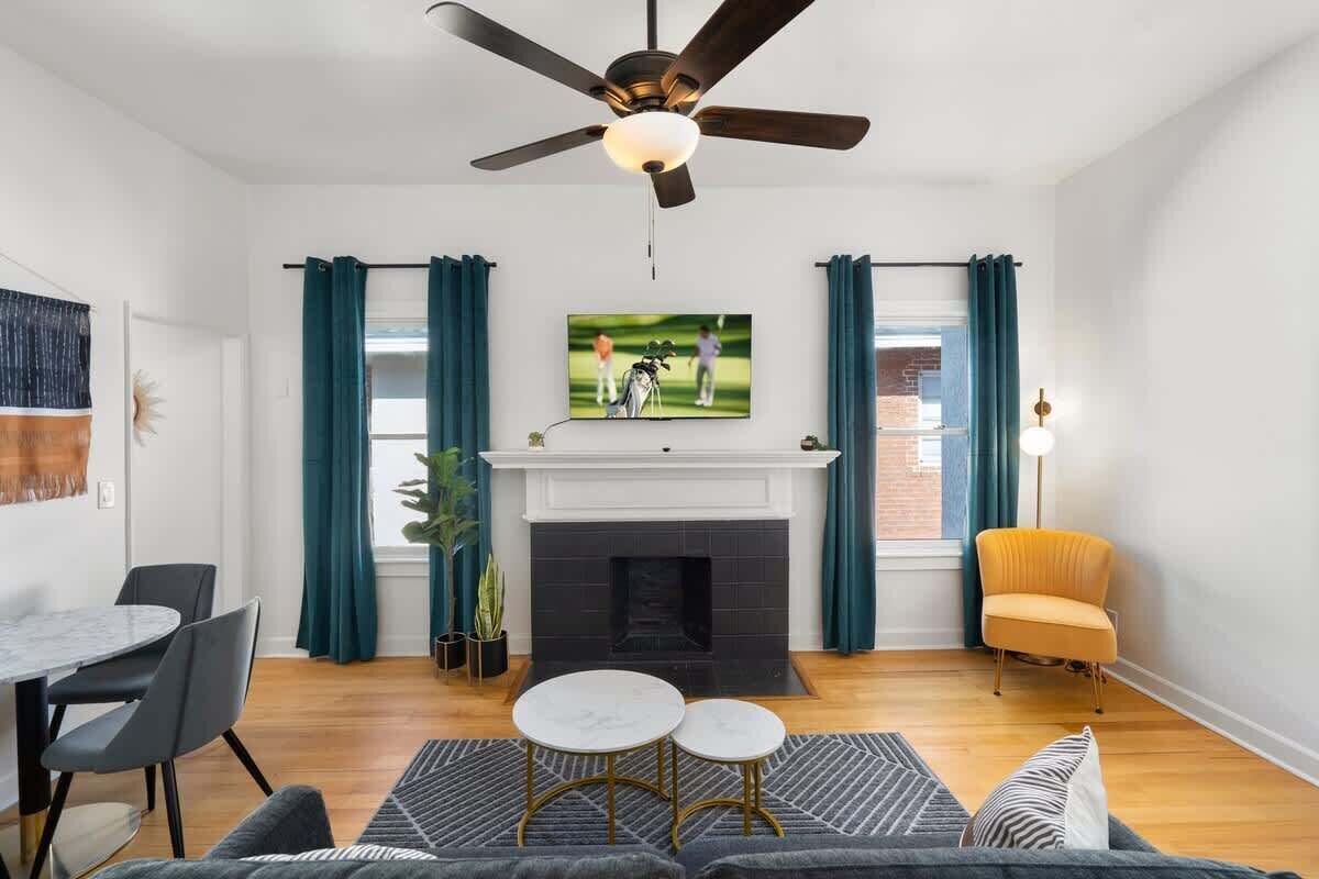 A living room with a fireplace, a ceiling fan, a television, and a dining area with chairs.