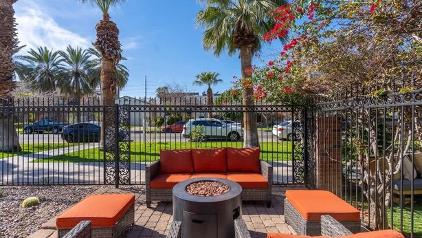 An outdoor patio with wicker furniture, a fire pit, and a view of a street with parked cars.