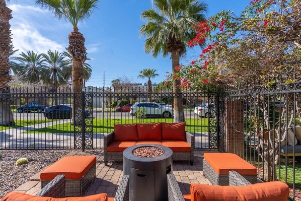 An outdoor patio with wicker furniture, a fire pit, and a view of a street with parked cars.