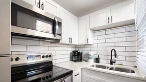 A kitchen with white cabinets, a stainless steel microwave, a black stove, and a coffee maker.