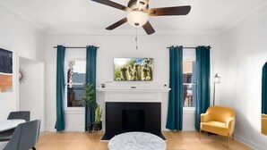A modern living room with a fireplace, a ceiling fan, and a television mounted above it.
