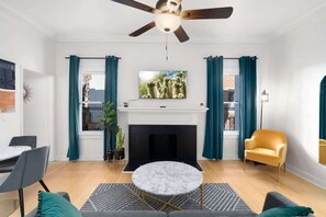 A modern living room with a fireplace, a ceiling fan, and a television mounted above it.