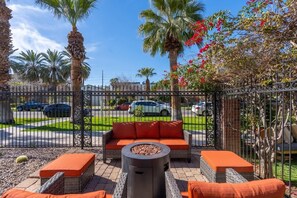 An outdoor patio with wicker furniture, a fire pit, and a view of a street with parked cars.