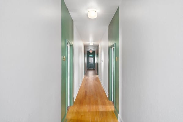 A hallway with a wooden floor and green walls, leading to a door at the end.