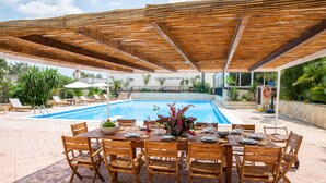 An outdoor pool area with a covered dining table and chairs, surrounded by lounge chairs and a stone wall. - Villa Palmizi with private pool, 6 bedrooms, 8 bathrooms in the heart of Salento (Ruffano)