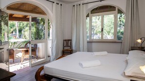 A bedroom with a large bed, a wooden chair, and a table by a sliding glass door leading to an outdoor area with chairs and a table. - Villa Palmizi with private pool, 6 bedrooms, 8 bathrooms in the heart of Salento (Ruffano)