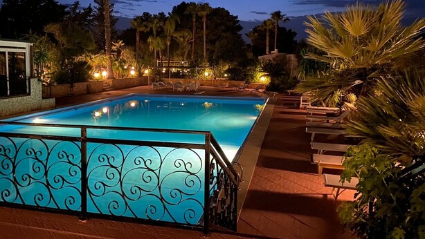 A rectangular swimming pool with a decorative metal fence, surrounded by palm trees and outdoor seating. - Villa Palmizi with private pool, 6 bedrooms, 8 bathrooms in the heart of Salento (Ruffano)