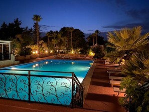 A rectangular swimming pool with a decorative metal fence, surrounded by palm trees and outdoor seating. - Villa Palmizi with a private pool, 6 bedrooms, and 8 bathrooms in the heart of Salento (Ruffano)