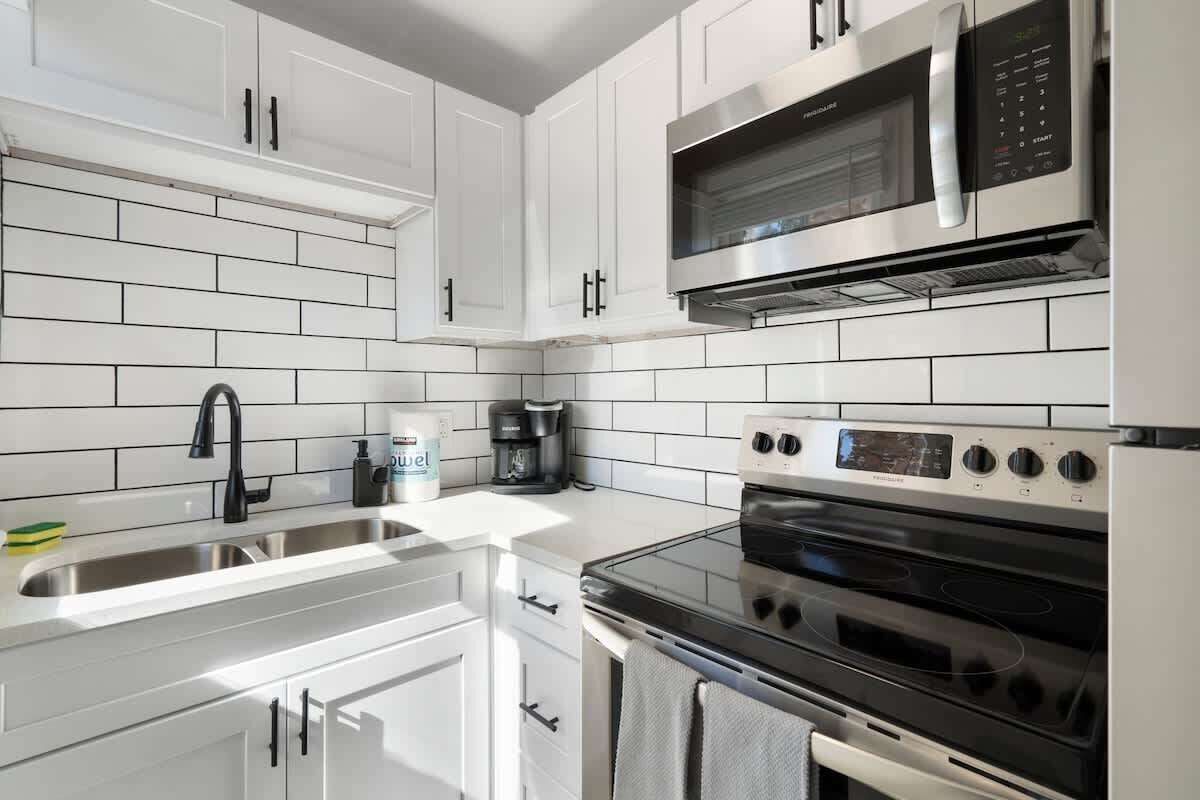 A modern kitchen with white cabinetry, a stainless steel sink, a microwave, and a built-in oven.