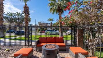 An outdoor patio with wicker furniture, a fire pit, and a view of a street with parked cars.