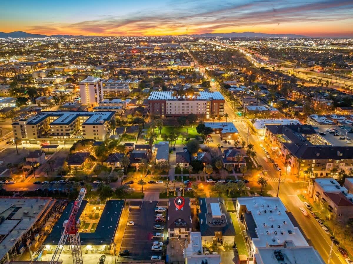 Vista aérea de um horizonte urbano ao entardecer, com um hotel imponente no centro, cercado por áreas residenciais e ruas.