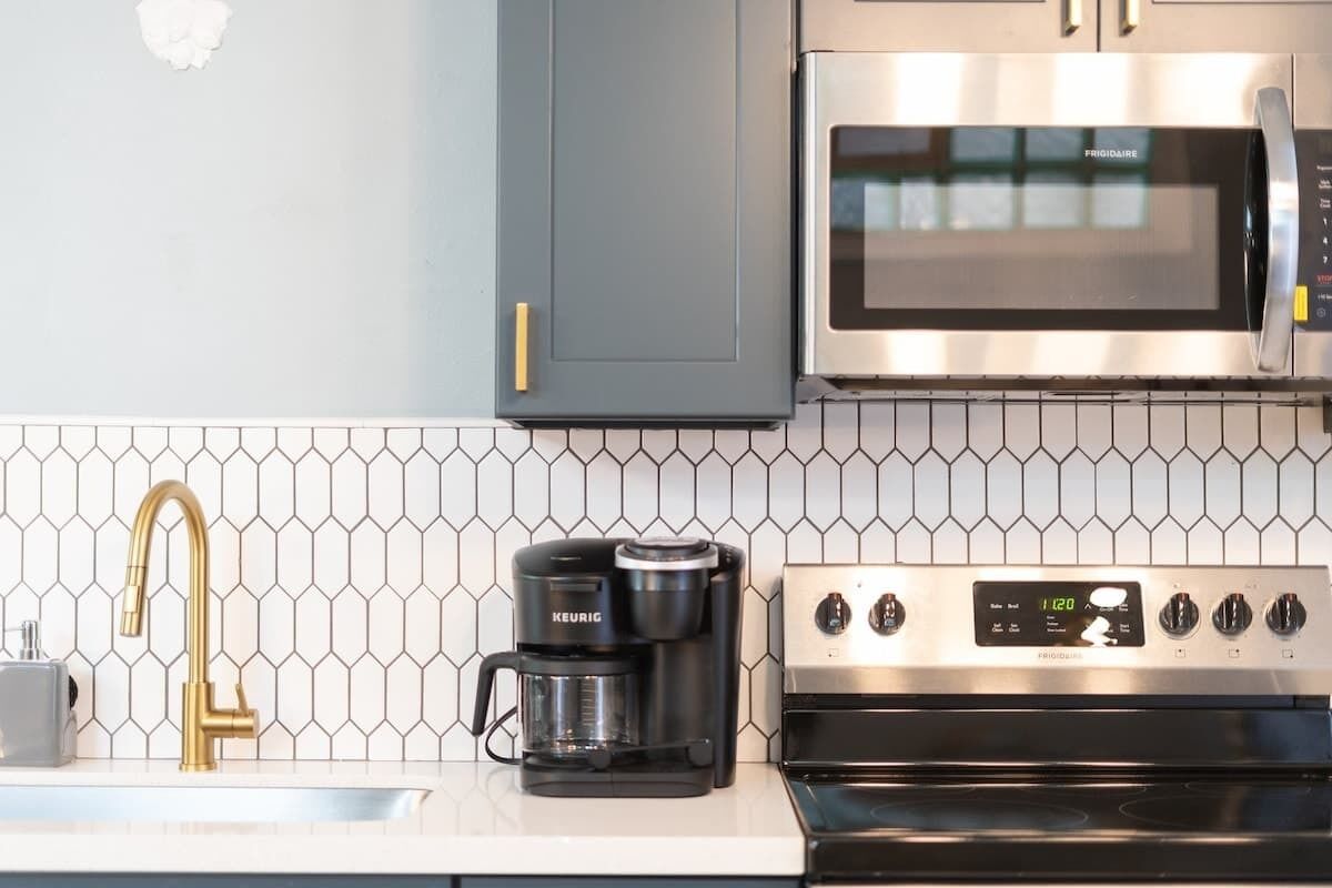 A kitchen with a stainless steel microwave, a coffee maker, and a sink with a gold faucet.