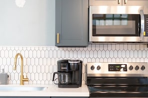 A kitchen with a stainless steel microwave, a coffee maker, and a sink with a gold faucet. - Modern Apartment in the Heart of Phoenix (10) (Phoenix)