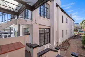 A two-story building with a balcony, a staircase, and a pathway leading to a garden area.