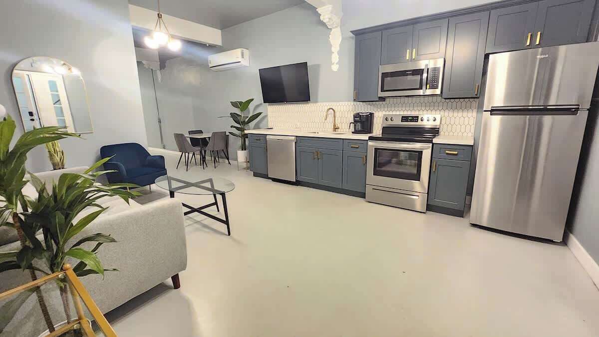 A modern kitchen with grey cabinets, stainless steel appliances, and a dining area with a blue chair and table.