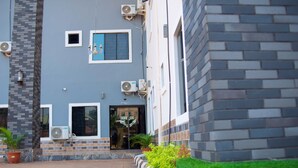 A hotel entrance with a blue door, air conditioning units, and potted plants.