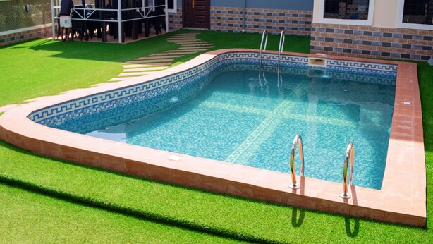 A swimming pool with a geometric tile pattern, surrounded by artificial grass and a brick border.