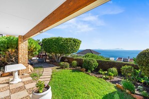A patio with a stone table, potted plants, and a view of the sea. - Zaria Sun Cottage (Cape Town)