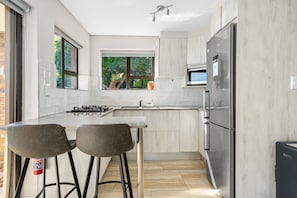 A modern kitchen with a central island, bar stools, a built-in oven, and a refrigerator.