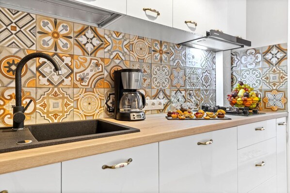 A kitchen with patterned tiles, a coffee maker, and a fruit bowl on the counter.