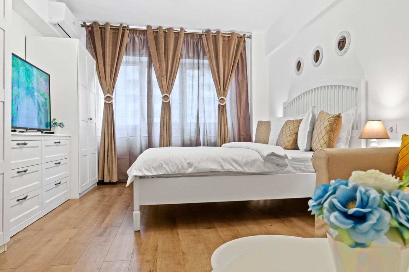Une chambre à coucher moderne avec un lit, une télévision, une commode et une table de chevet agrémentée de fleurs.