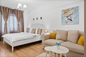 A bedroom with a bed, a sofa, a nightstand, and a painting.