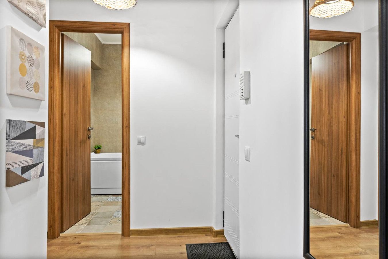 Ein Korridor mit Holztüren, einer weißen Wand und einem gefliesten Boden.