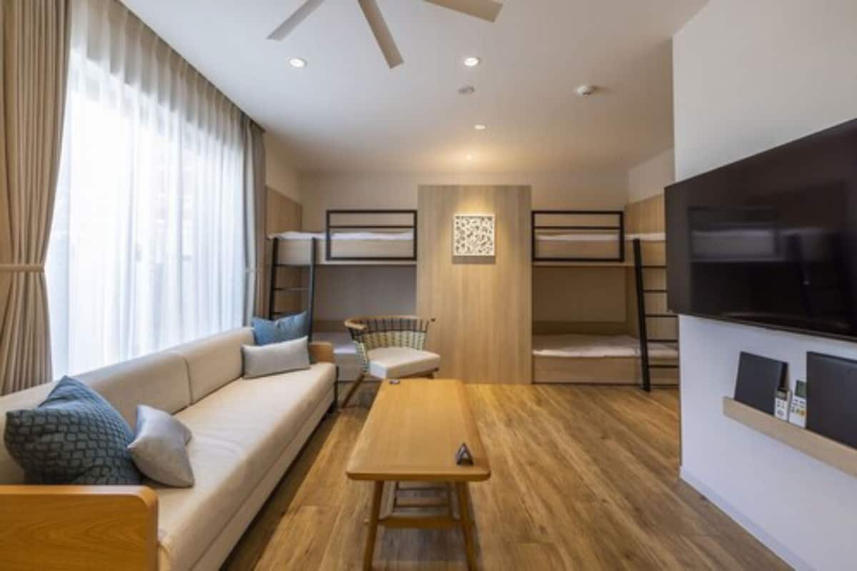 A modern hotel room with a sofa, a wooden table, a TV, and bunk beds.