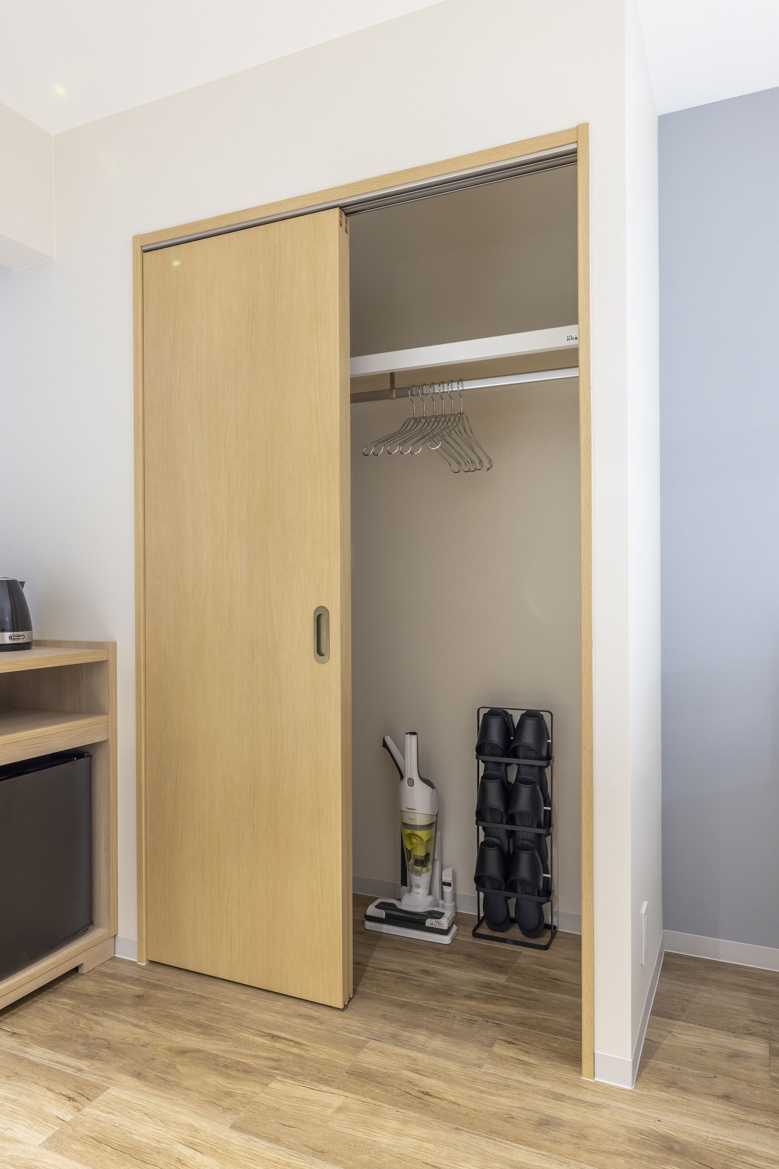 A room with a wooden wardrobe, a shoe rack, and a vacuum cleaner.