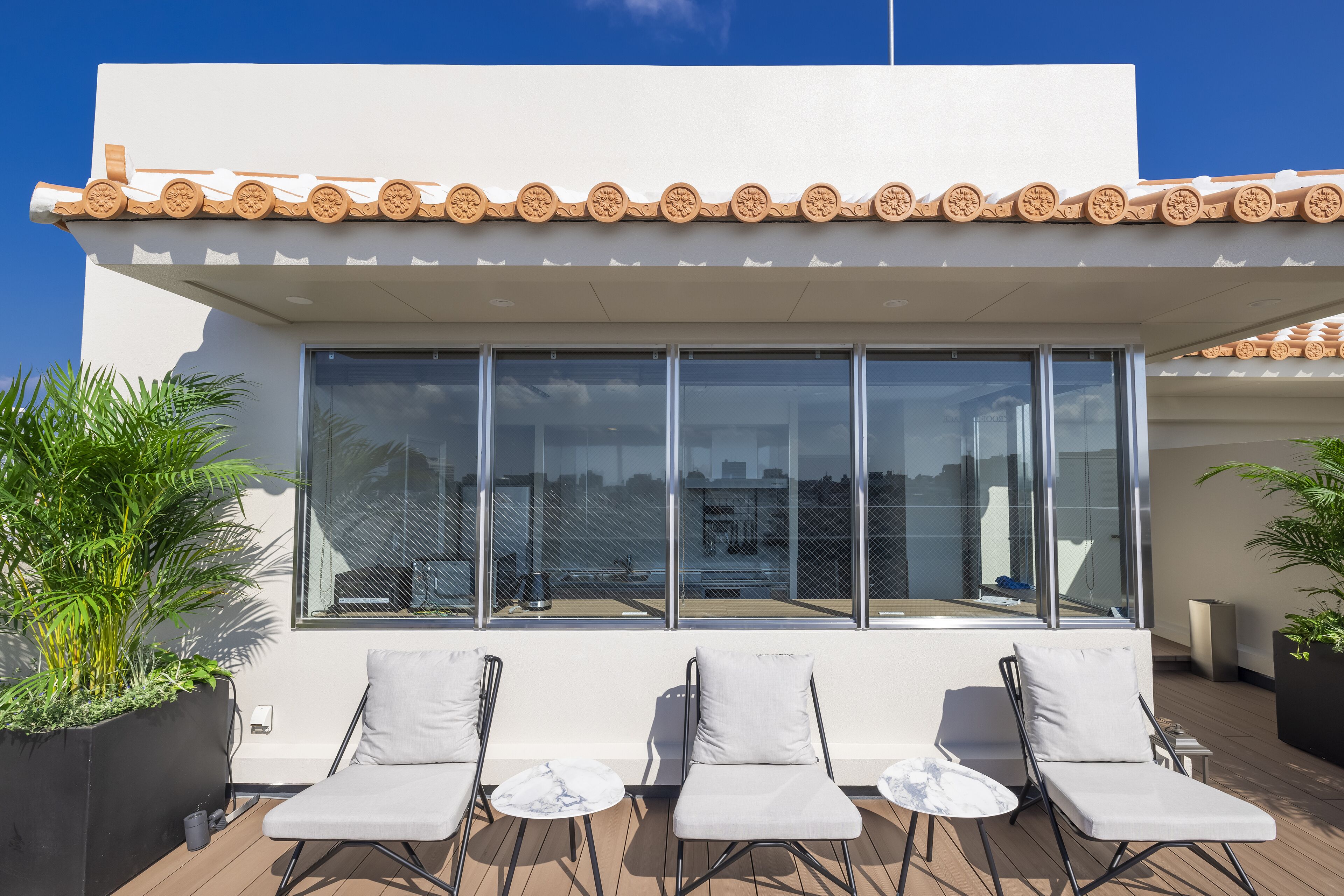 A rooftop terrace with four lounge chairs and a large window overlooking the city.