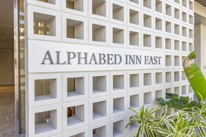 A sign for Alphabed Inn East with a grid-like structure and potted plants in front.