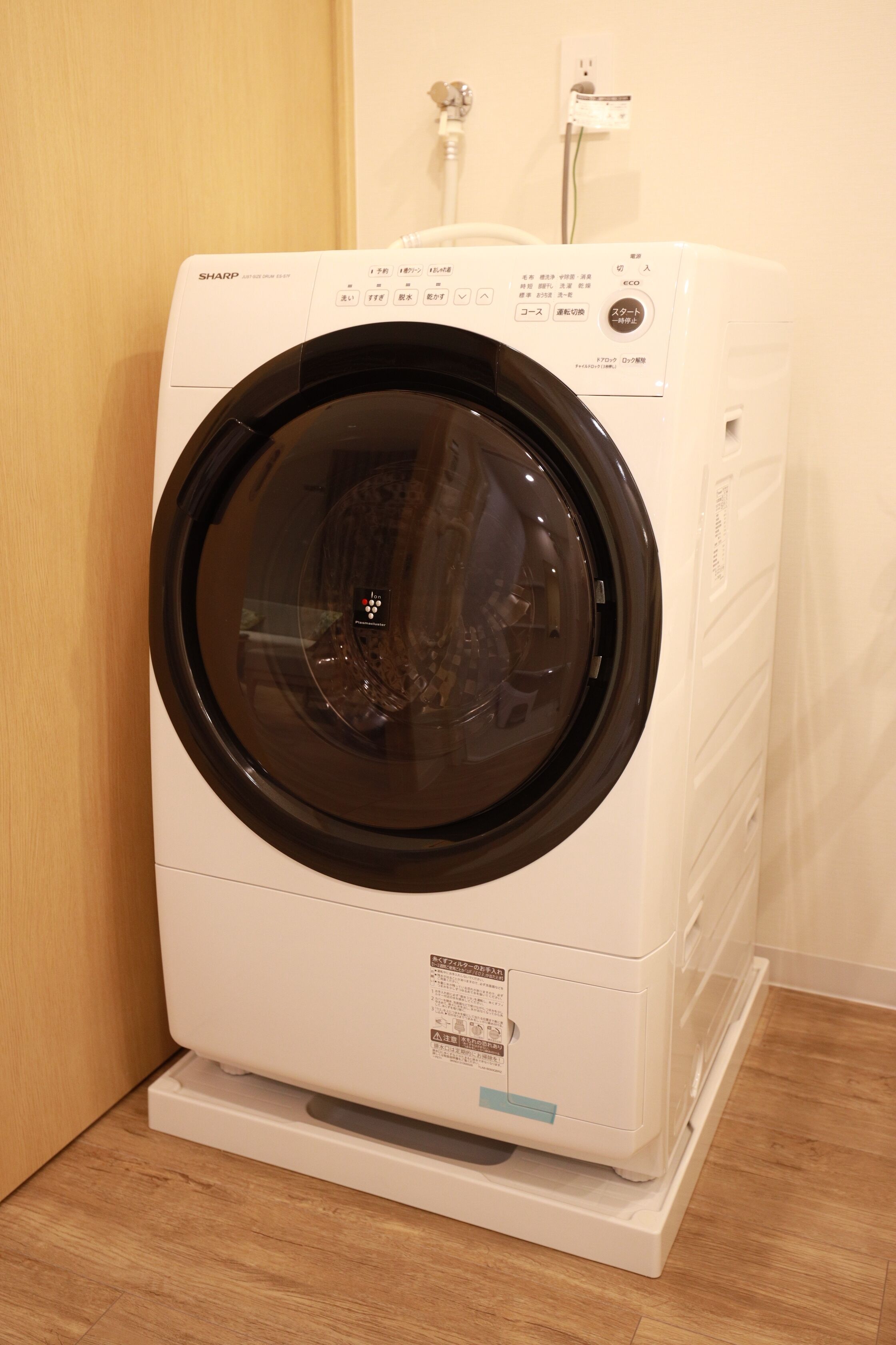 A front-loading washing machine in a room with a wooden floor and a white wall.