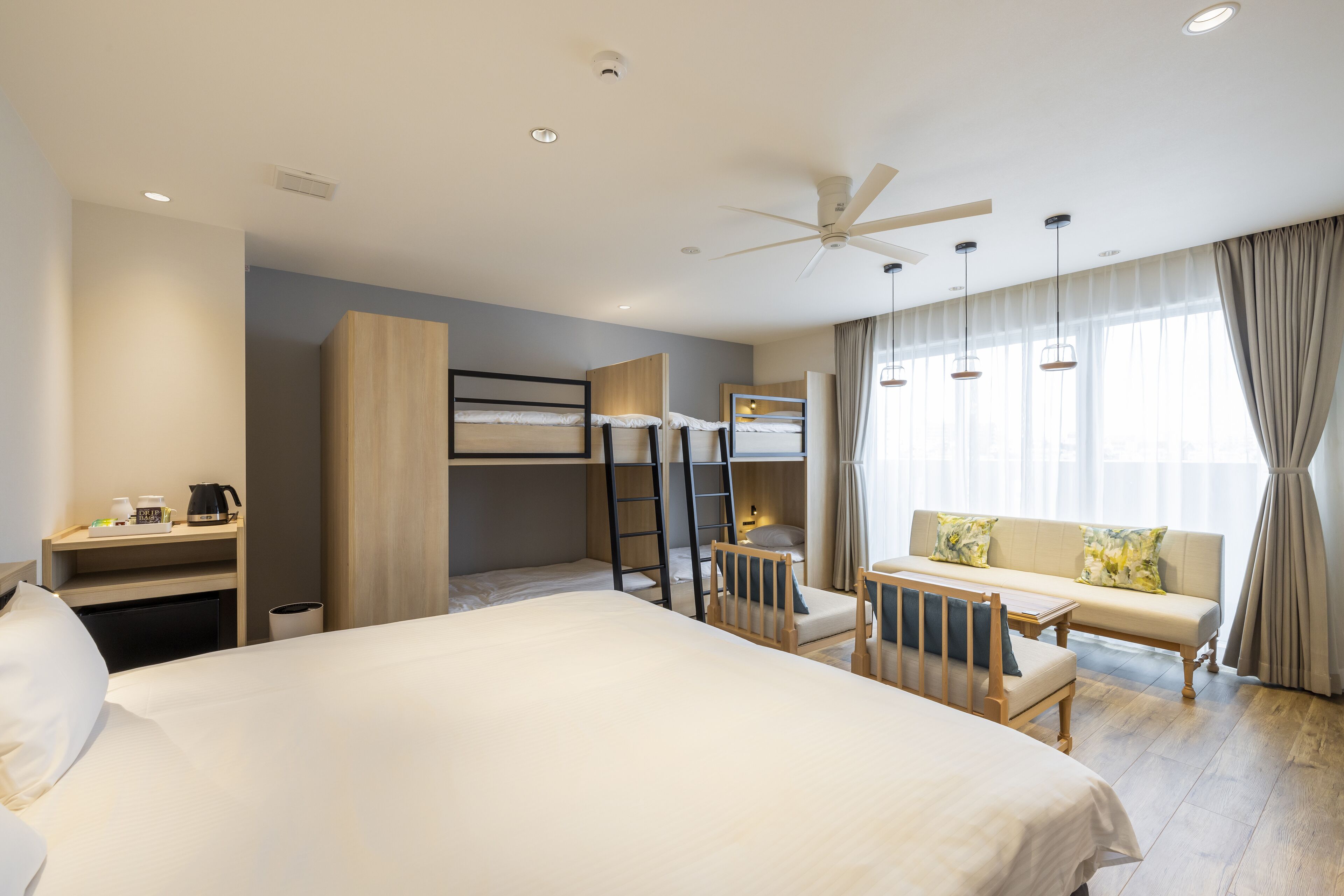Une chambre d’hôtel avec un grand lit, un bureau avec une chaise, un canapé, un lit superposé et un ventilateur de plafond.