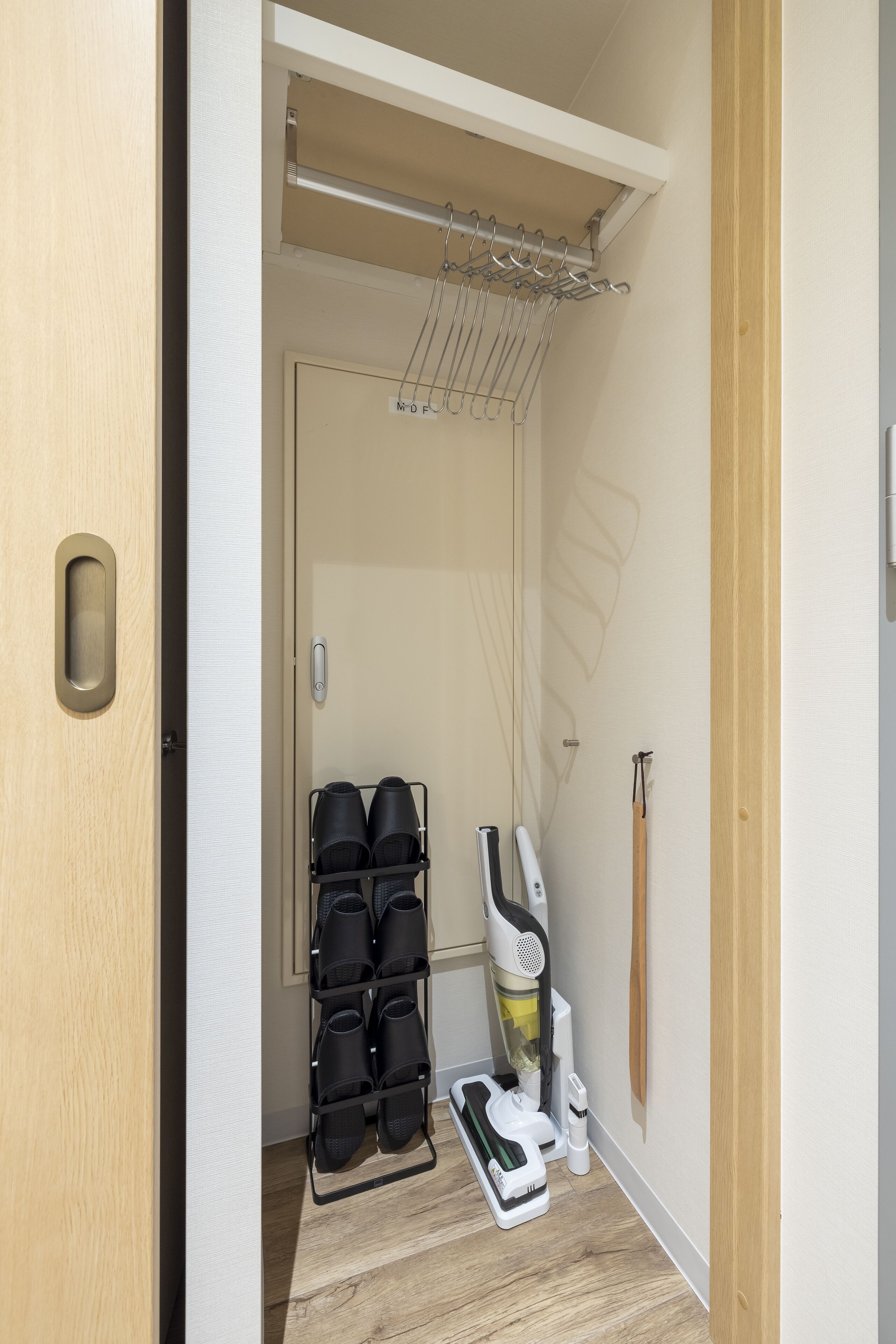 A hallway with a shoe rack, a vacuum cleaner, and a broom.