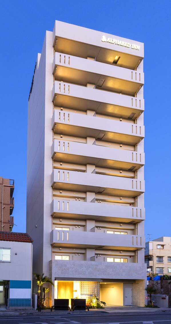 A multi-story hotel with a modern design, featuring balconies on each floor, a prominent signage at the top, and a well-lit entrance.