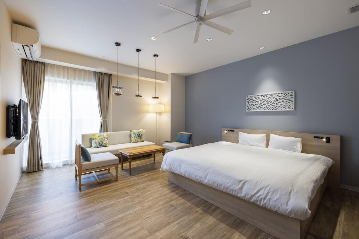 A modern hotel room with a large bed, a sofa, a desk, and a ceiling fan.